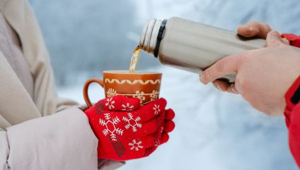 person pouring hot beverage for another person in winter weather