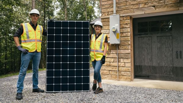 two lightwave employees holding up large solar panel in front of customer home